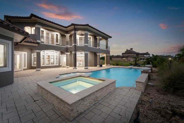 back house at dusk featuring a patio area, a balcony, and a swimming pool with hot tub