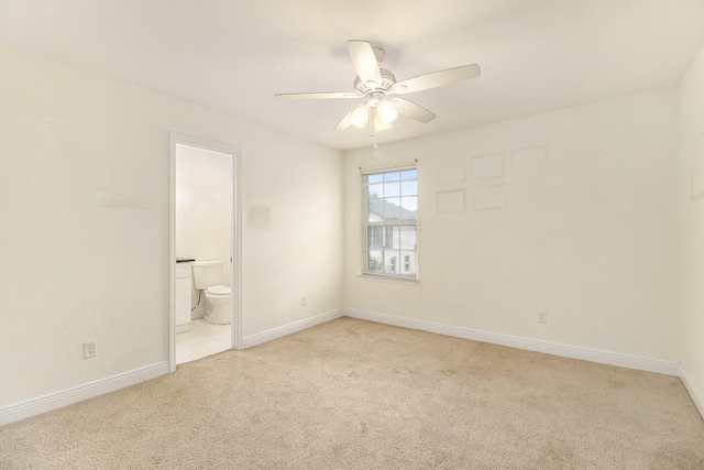 unfurnished bedroom featuring baseboards, ensuite bathroom, light carpet, and a ceiling fan