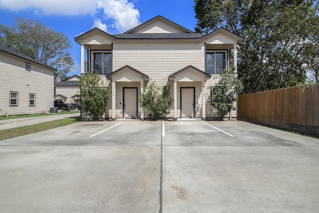 traditional home with fence, roof with shingles, uncovered parking, and a balcony