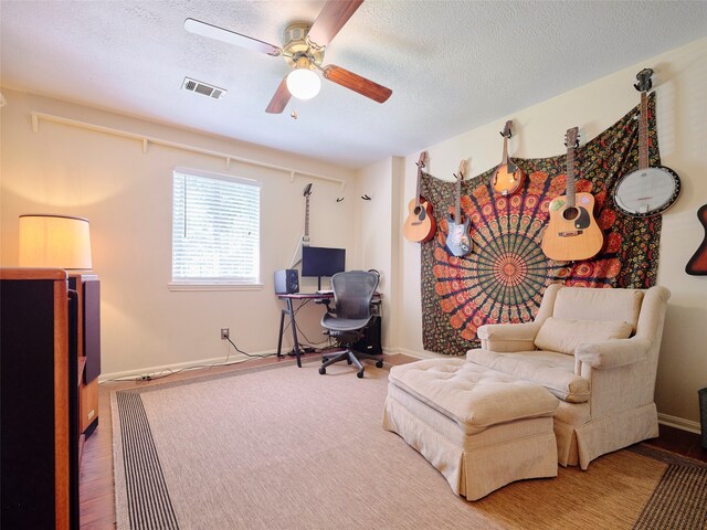 sitting room with ceiling fan, wood-type flooring, and a textured ceiling