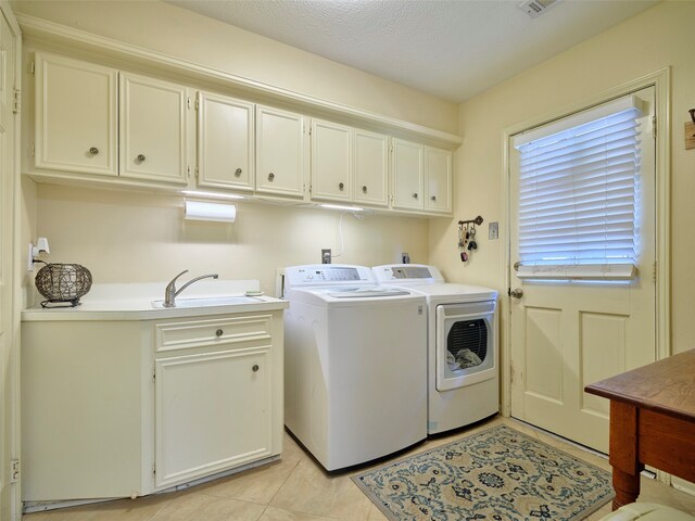 laundry room with cabinets, a textured ceiling, sink, washing machine and dryer, and light tile patterned flooring