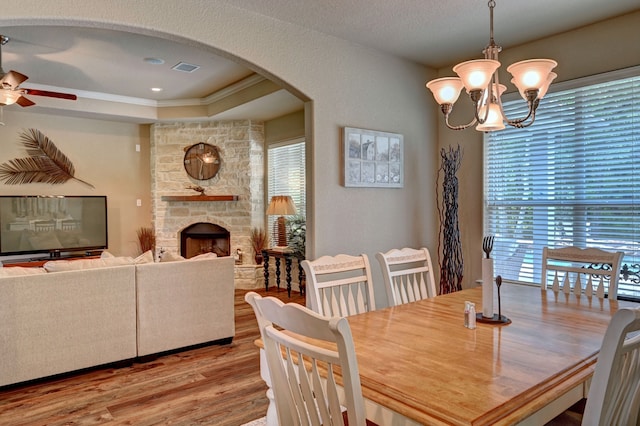 dining room featuring a healthy amount of sunlight, ceiling fan with notable chandelier, a stone fireplace, and light hardwood / wood-style flooring