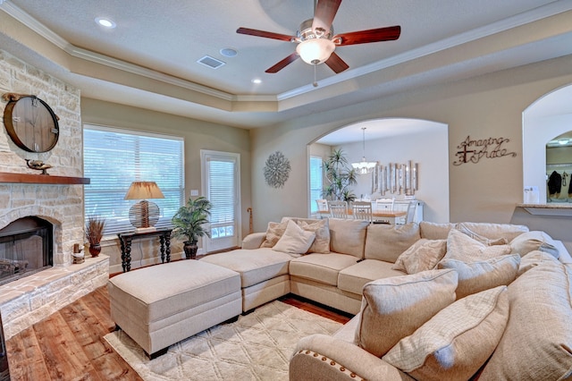 living room with ceiling fan, a raised ceiling, ornamental molding, a fireplace, and light wood-type flooring