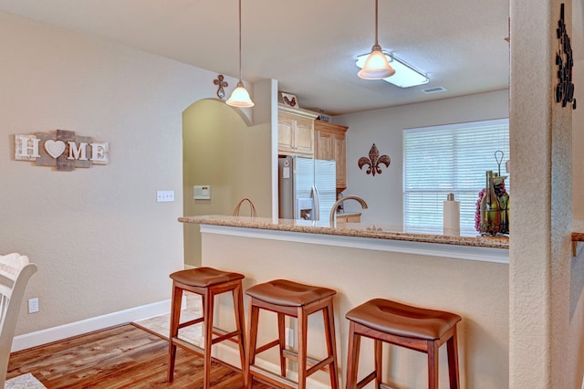 kitchen with light stone countertops, pendant lighting, light hardwood / wood-style flooring, stainless steel refrigerator with ice dispenser, and sink