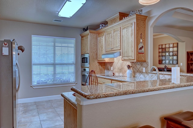 kitchen with light stone countertops, stainless steel appliances, kitchen peninsula, and light brown cabinetry