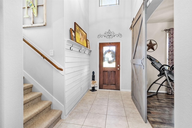 entryway featuring baseboards, light tile patterned flooring, stairs, a towering ceiling, and a barn door