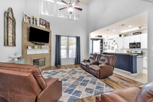 living room with a ceiling fan, light wood-style floors, a towering ceiling, and a fireplace