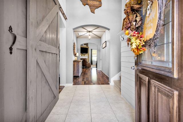 tiled entrance foyer featuring a barn door, wooden walls, and arched walkways