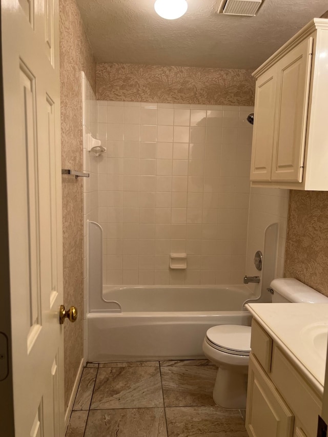 full bathroom featuring a textured ceiling, vanity, toilet, and tiled shower / bath