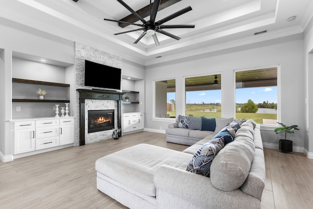 living room with light hardwood / wood-style floors, a fireplace, a raised ceiling, ceiling fan, and built in features