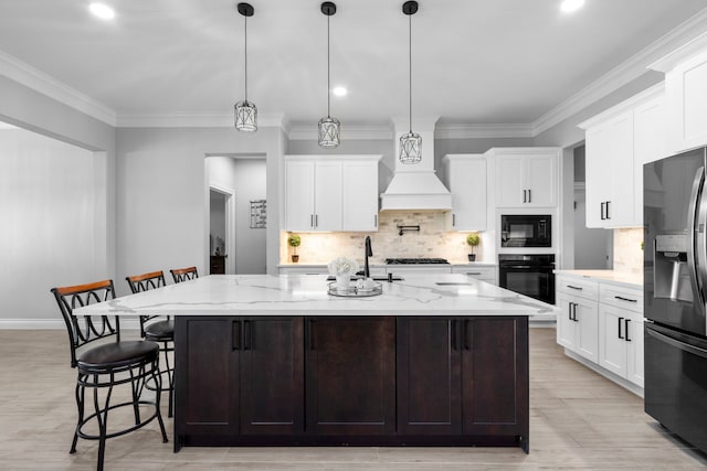 kitchen with black appliances, a kitchen island with sink, light stone countertops, and pendant lighting