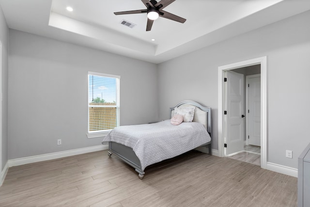 bedroom featuring light wood-type flooring, ceiling fan, and a raised ceiling