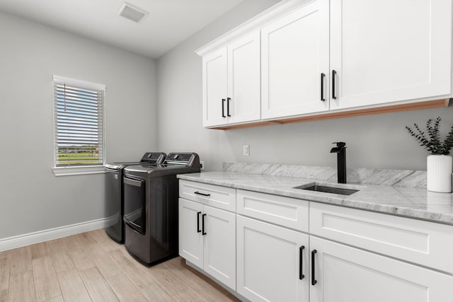 laundry area featuring washer and clothes dryer, cabinets, light wood-type flooring, and sink