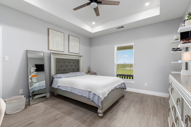 bedroom with light wood-type flooring, a tray ceiling, and ceiling fan