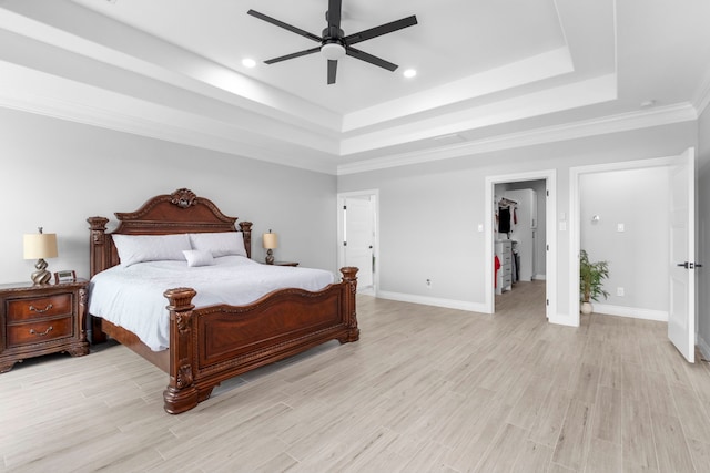 bedroom featuring light wood-type flooring, a raised ceiling, a walk in closet, crown molding, and ceiling fan