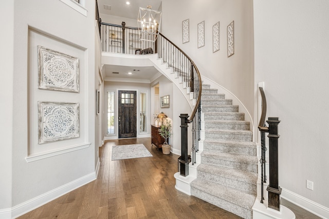 entryway with crown molding, a towering ceiling, dark hardwood / wood-style floors, and an inviting chandelier