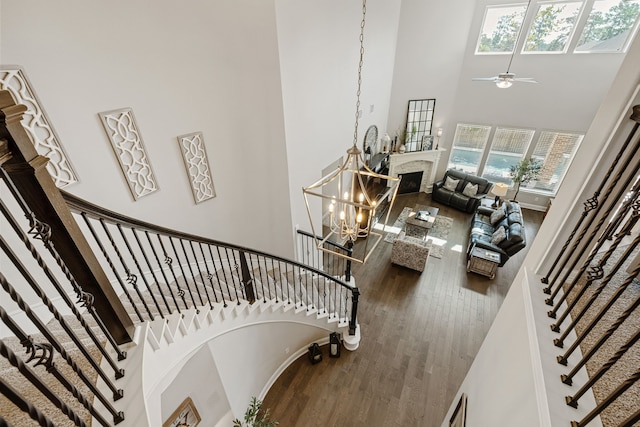 stairs with ceiling fan with notable chandelier, wood-type flooring, and a towering ceiling