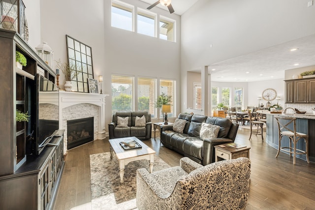 living room featuring ceiling fan, dark hardwood / wood-style flooring, a stone fireplace, and a high ceiling