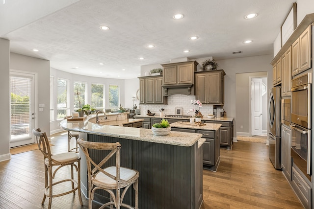 kitchen featuring light stone countertops, kitchen peninsula, dark hardwood / wood-style flooring, multiple ovens, and a kitchen island