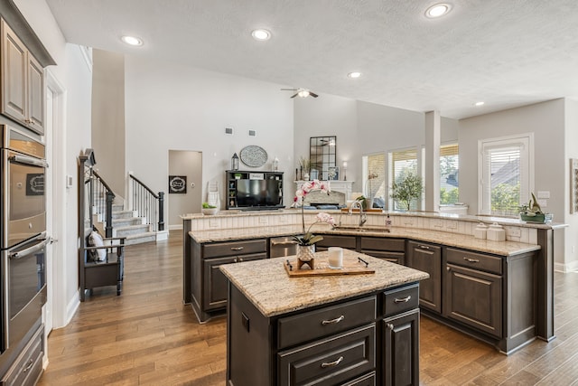 kitchen featuring dark brown cabinetry, light stone countertops, a center island, sink, and appliances with stainless steel finishes