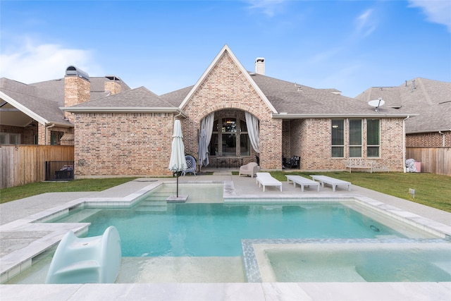 rear view of property featuring a patio and a swimming pool with hot tub