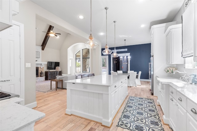 kitchen with sink, vaulted ceiling with beams, a kitchen island, hanging light fixtures, and white cabinets