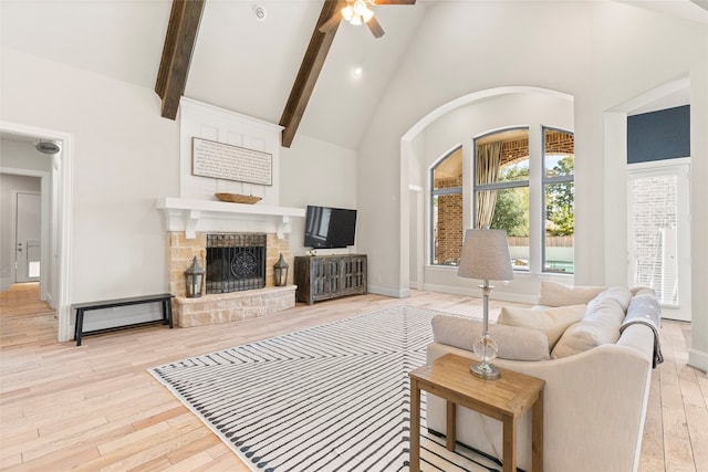 living room with a stone fireplace, beam ceiling, light wood-type flooring, high vaulted ceiling, and ceiling fan