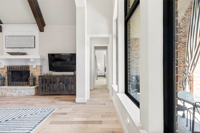 living room with beam ceiling, light hardwood / wood-style flooring, a fireplace, and a healthy amount of sunlight