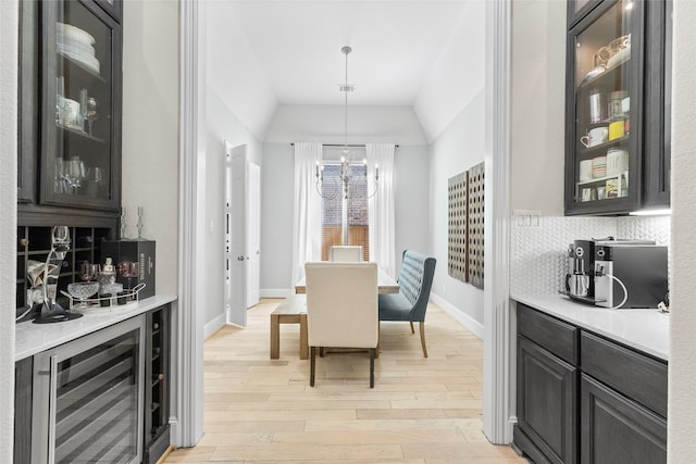 dining space featuring lofted ceiling, light hardwood / wood-style flooring, a notable chandelier, bar area, and beverage cooler