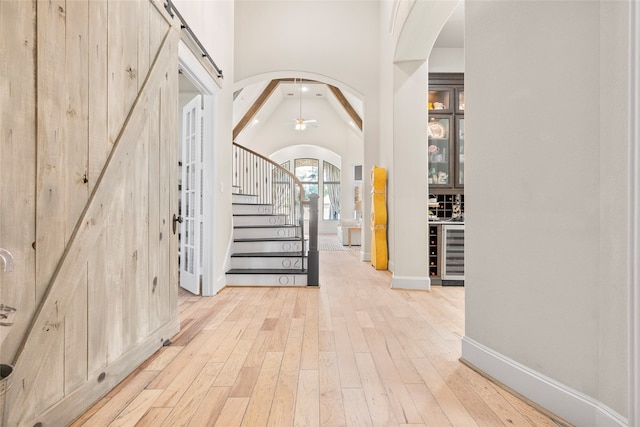 entryway with wine cooler, lofted ceiling with beams, a barn door, light wood-type flooring, and ceiling fan