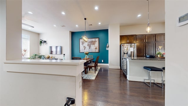 kitchen featuring pendant lighting, dark hardwood / wood-style floors, kitchen peninsula, dark brown cabinetry, and stainless steel fridge