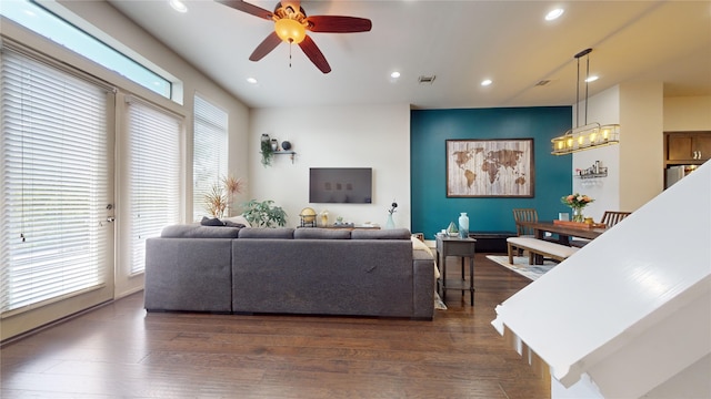 living room with ceiling fan with notable chandelier, plenty of natural light, and dark wood-type flooring