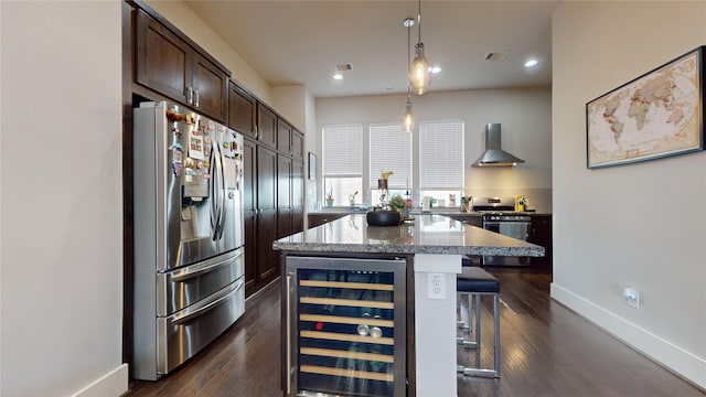 kitchen featuring stainless steel fridge, a breakfast bar, wall chimney exhaust hood, a center island, and beverage cooler