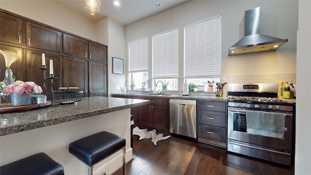 kitchen with appliances with stainless steel finishes, dark stone countertops, dark brown cabinets, range hood, and dark hardwood / wood-style floors