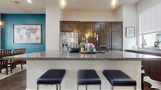 kitchen featuring a breakfast bar, a center island, dark hardwood / wood-style floors, stainless steel fridge with ice dispenser, and stone counters