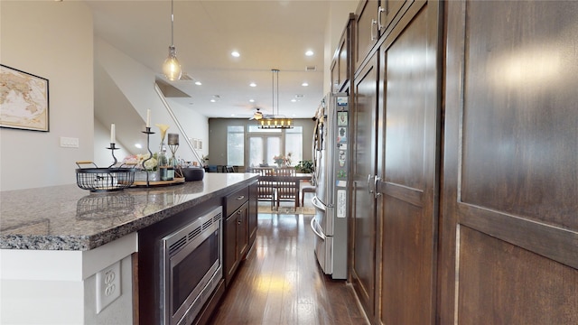 kitchen with pendant lighting, dark brown cabinets, dark hardwood / wood-style floors, appliances with stainless steel finishes, and dark stone countertops