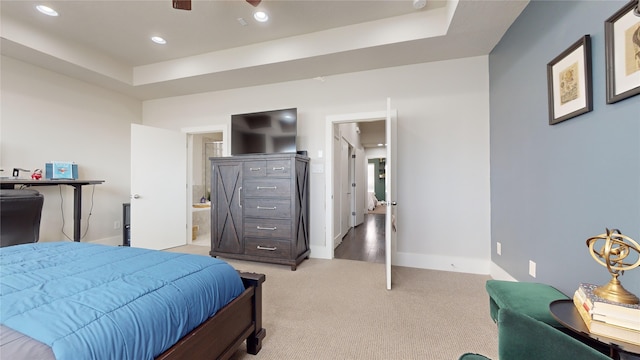 bedroom featuring connected bathroom, a tray ceiling, ceiling fan, and light carpet