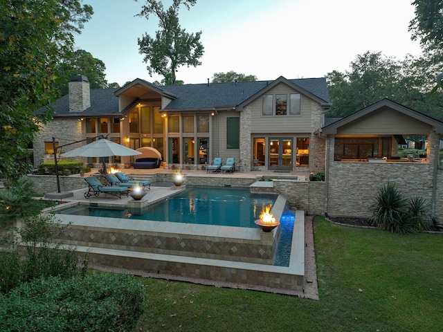 back of property with a swimming pool with hot tub, a lawn, and a patio area