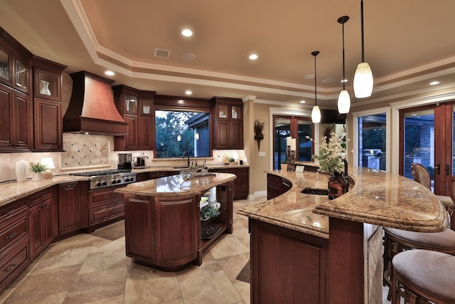 kitchen featuring a kitchen island with sink, hanging light fixtures, custom exhaust hood, decorative backsplash, and a raised ceiling