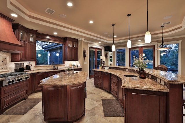 kitchen featuring hanging light fixtures, tasteful backsplash, a tray ceiling, a large island, and sink