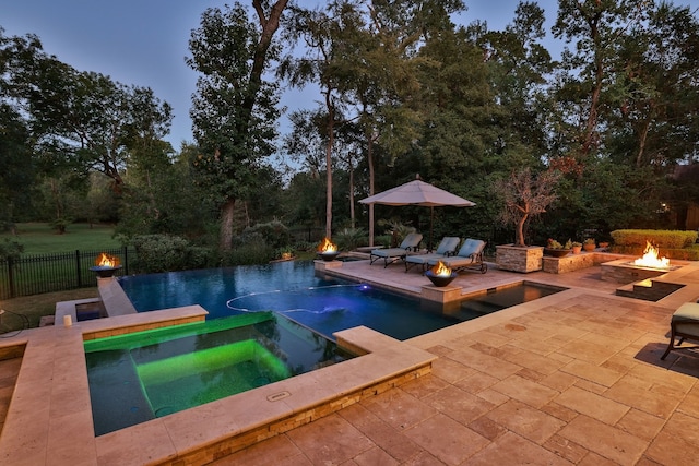 pool at dusk featuring a patio, an in ground hot tub, and an outdoor fire pit