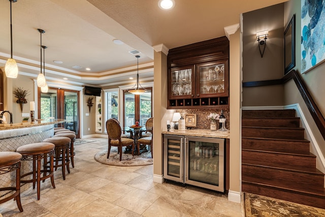 bar with dark brown cabinets, wine cooler, light stone countertops, and decorative light fixtures