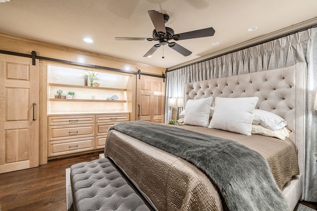 bedroom featuring dark hardwood / wood-style flooring, a textured ceiling, ceiling fan, and a barn door