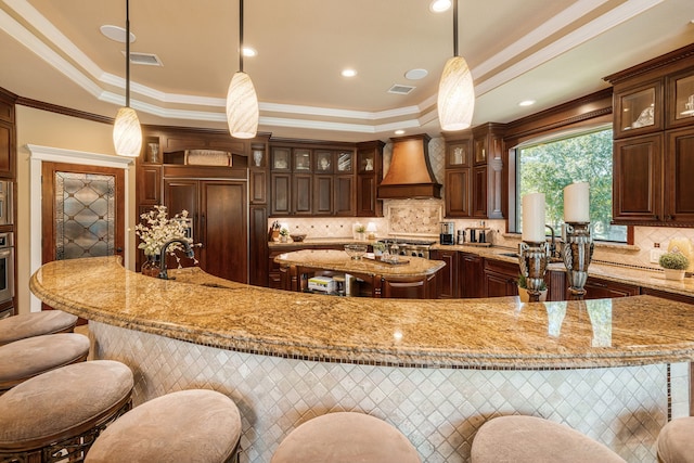 kitchen featuring sink, a raised ceiling, hanging light fixtures, and custom range hood