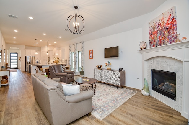 living room with a tile fireplace, an inviting chandelier, and light hardwood / wood-style flooring