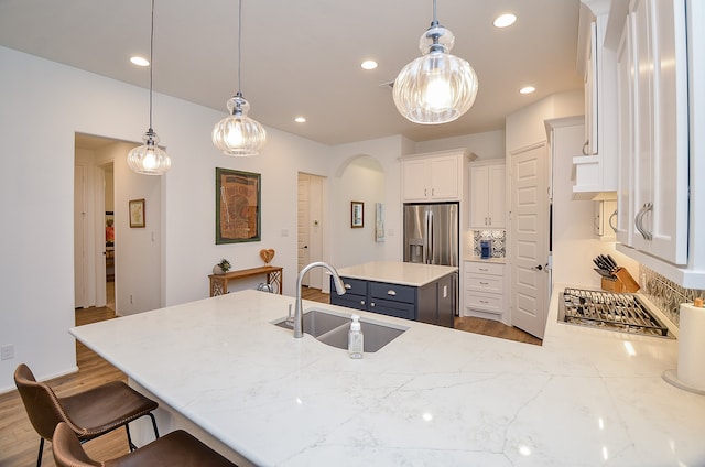 kitchen with white cabinets, stainless steel fridge, sink, and pendant lighting