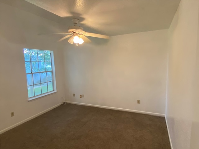 empty room with ceiling fan and dark colored carpet