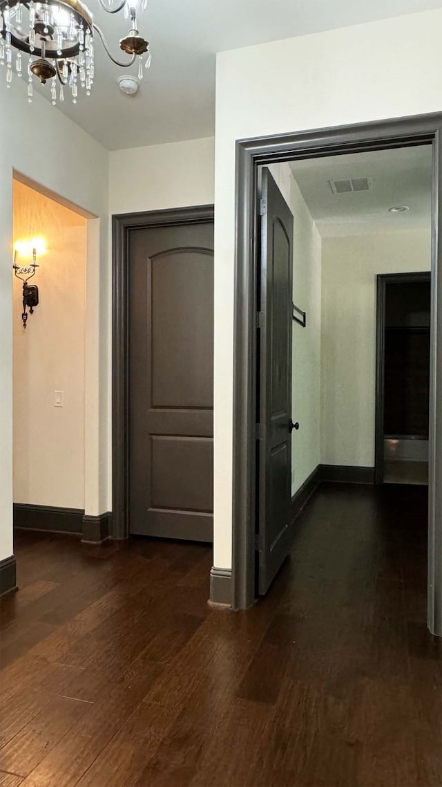 corridor with dark hardwood / wood-style floors and a notable chandelier