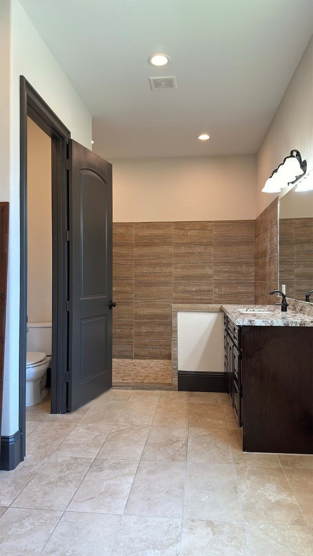 bathroom with vanity, toilet, and tile walls