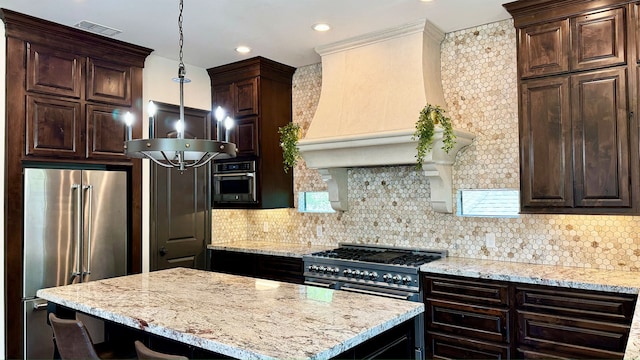 kitchen featuring tasteful backsplash, high quality appliances, custom range hood, and decorative light fixtures